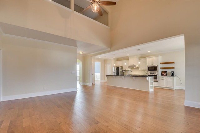 unfurnished living room with a towering ceiling, sink, ceiling fan, and light hardwood / wood-style flooring