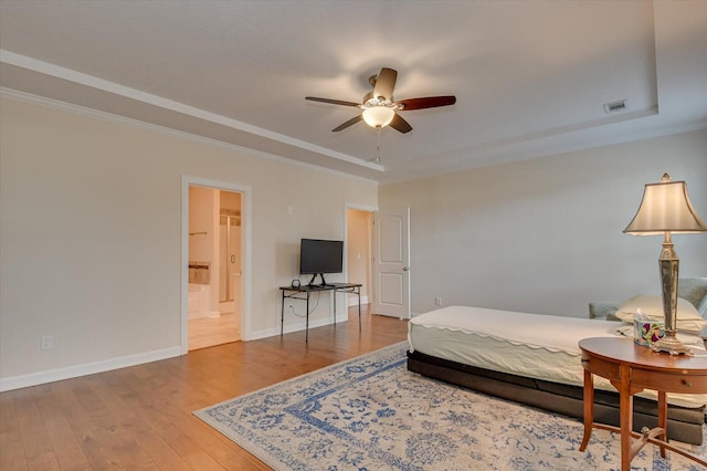 bedroom with ensuite bathroom, wood-type flooring, ornamental molding, ceiling fan, and a raised ceiling