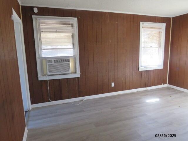 empty room featuring cooling unit, wooden walls, baseboards, and wood finished floors