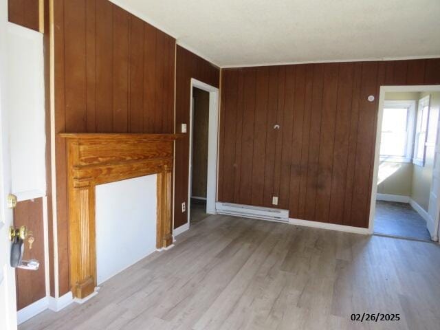 empty room with light wood-type flooring, wood walls, a baseboard radiator, and baseboards