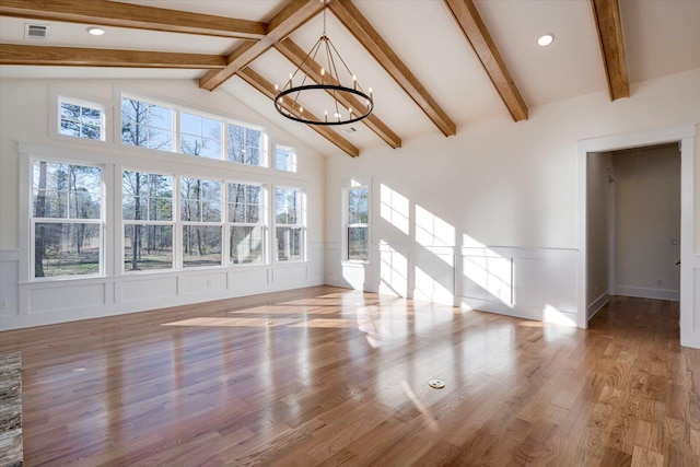 unfurnished living room featuring beamed ceiling, a healthy amount of sunlight, light wood-type flooring, and a chandelier