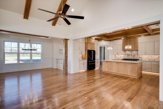 kitchen with decorative light fixtures, ceiling fan, light hardwood / wood-style floors, and a kitchen island with sink