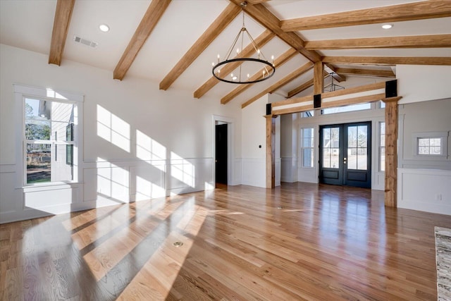 unfurnished living room featuring light hardwood / wood-style floors, beam ceiling, french doors, and an inviting chandelier