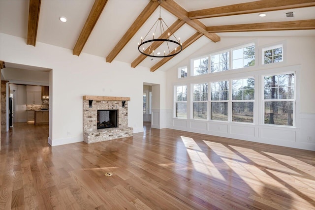 unfurnished living room featuring a brick fireplace, light hardwood / wood-style flooring, beamed ceiling, high vaulted ceiling, and a chandelier