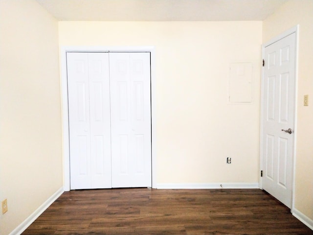 unfurnished bedroom featuring dark wood-type flooring, a closet, baseboards, and electric panel