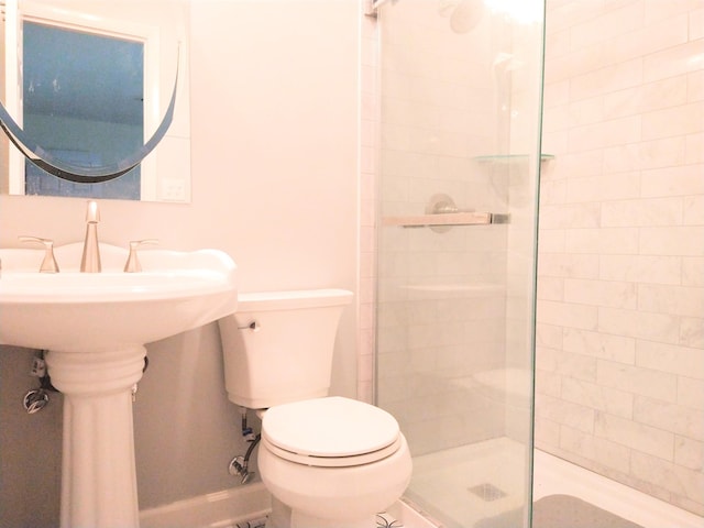 bathroom with a tile shower, toilet, and baseboards