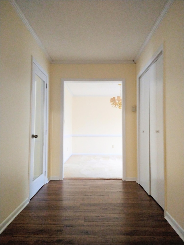 hallway featuring dark wood-style flooring, crown molding, a chandelier, and baseboards