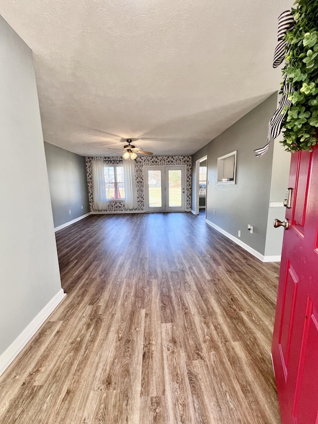 unfurnished living room featuring wood finished floors, baseboards, ceiling fan, and a textured ceiling