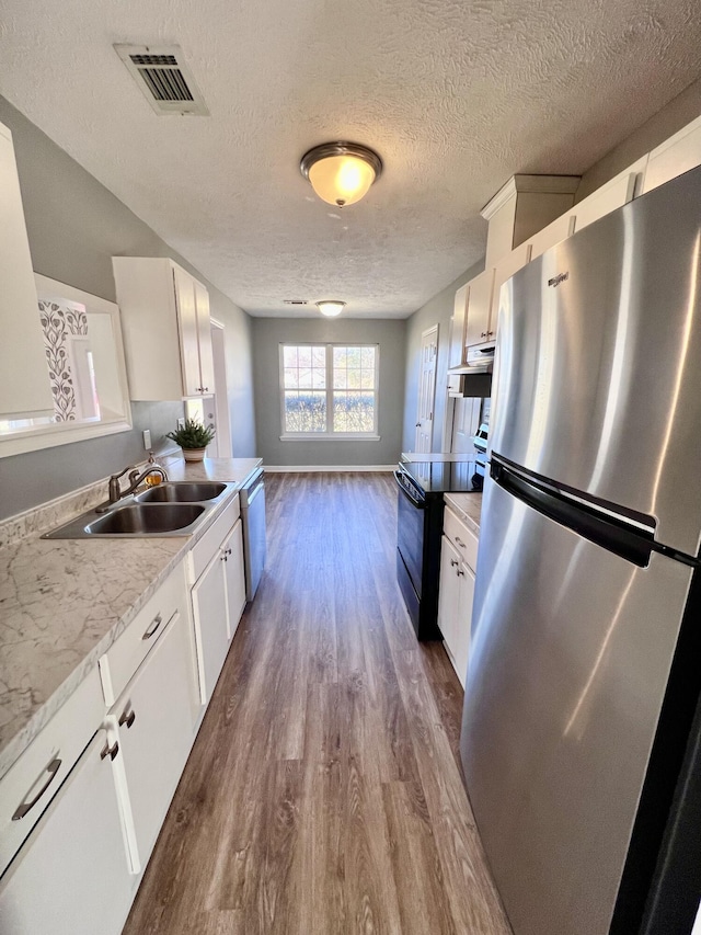 kitchen with stainless steel appliances, a sink, under cabinet range hood, dark wood-type flooring, and a textured ceiling
