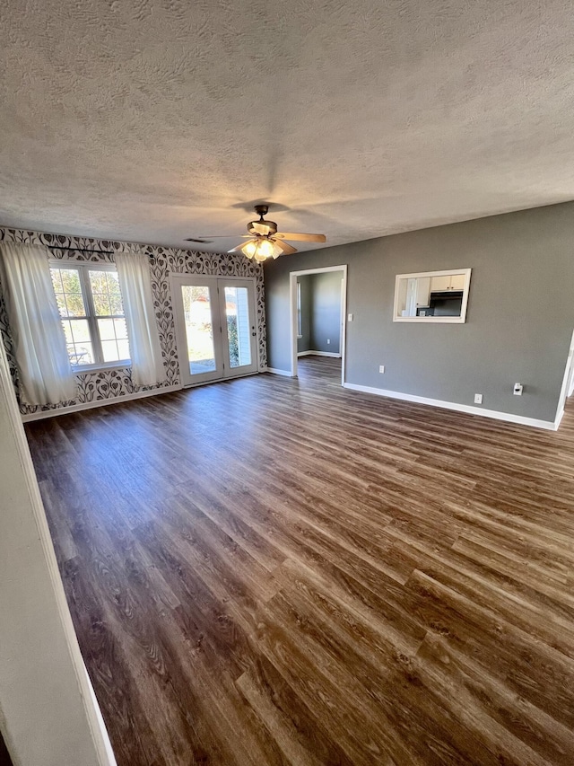 unfurnished living room with a textured ceiling, baseboards, dark wood-style flooring, a ceiling fan, and french doors