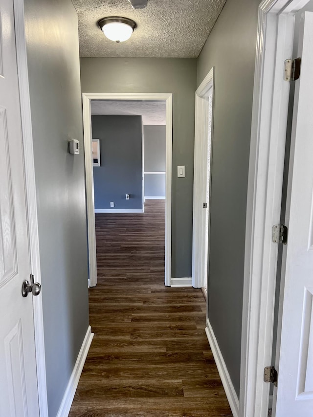 hall featuring dark wood-type flooring, baseboards, and a textured ceiling