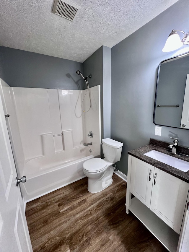 bathroom featuring wood finished floors, toilet, a textured ceiling, tub / shower combination, and vanity