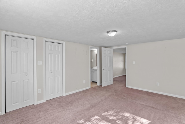 unfurnished bedroom featuring two closets, connected bathroom, a textured ceiling, and light colored carpet