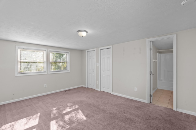 unfurnished bedroom featuring two closets, connected bathroom, light carpet, and a textured ceiling