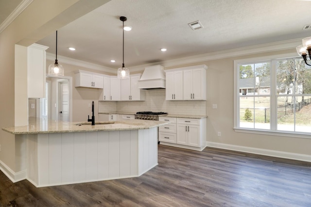 kitchen with custom exhaust hood, a peninsula, light stone countertops, and a sink