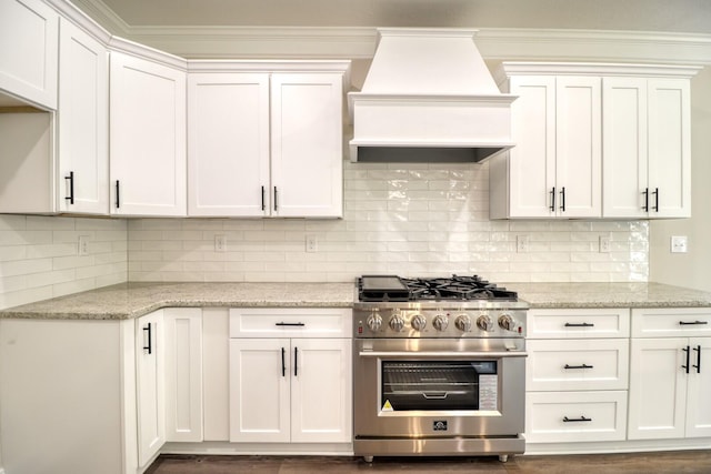 kitchen featuring light stone countertops, decorative backsplash, custom range hood, white cabinets, and high end stainless steel range