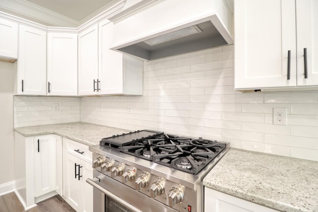 kitchen featuring wood finished floors, premium range hood, stainless steel range with gas stovetop, decorative backsplash, and white cabinets