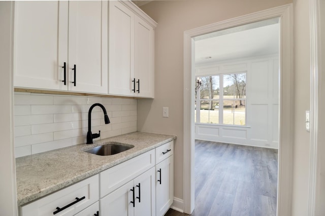 kitchen with a sink, light stone counters, tasteful backsplash, wood finished floors, and white cabinetry