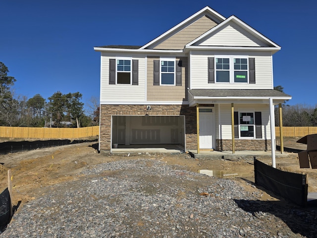 view of front of home with an attached garage, fence, covered porch, stone siding, and driveway