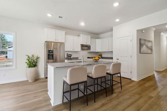 kitchen with a center island with sink, a kitchen breakfast bar, stainless steel appliances, light wood-style floors, and white cabinets