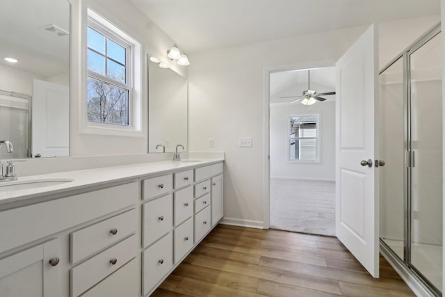 full bathroom featuring double vanity, a stall shower, wood finished floors, and a sink