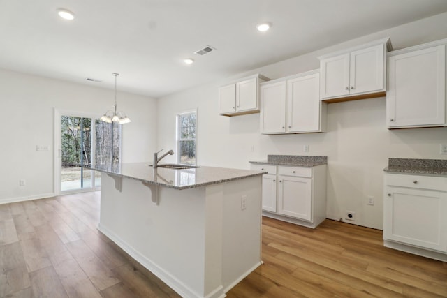 kitchen with light stone counters, visible vents, light wood finished floors, and a sink