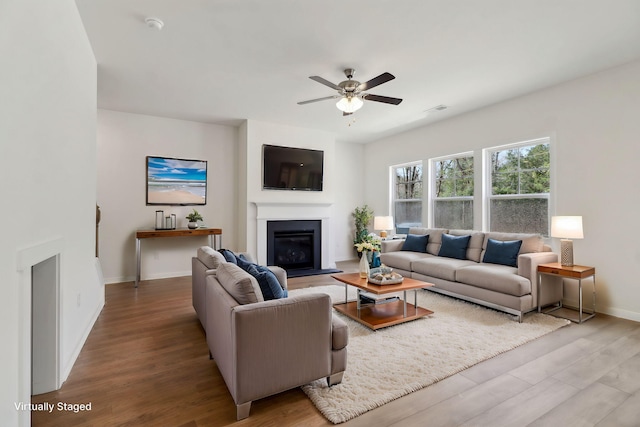 living room with visible vents, a glass covered fireplace, wood finished floors, baseboards, and ceiling fan