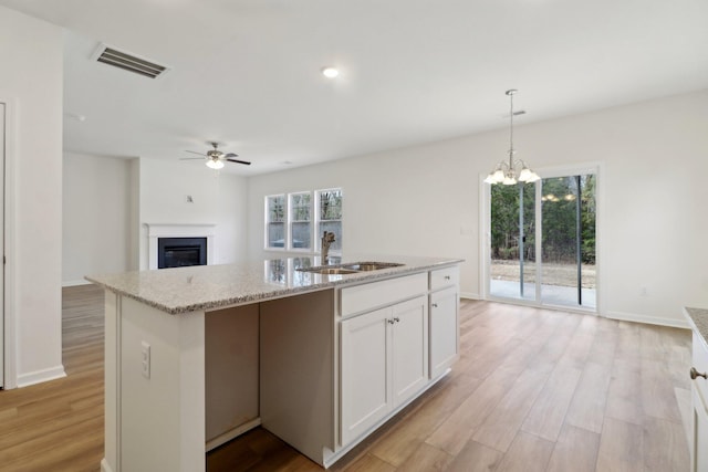 kitchen with a glass covered fireplace, light wood-style flooring, visible vents, and a sink