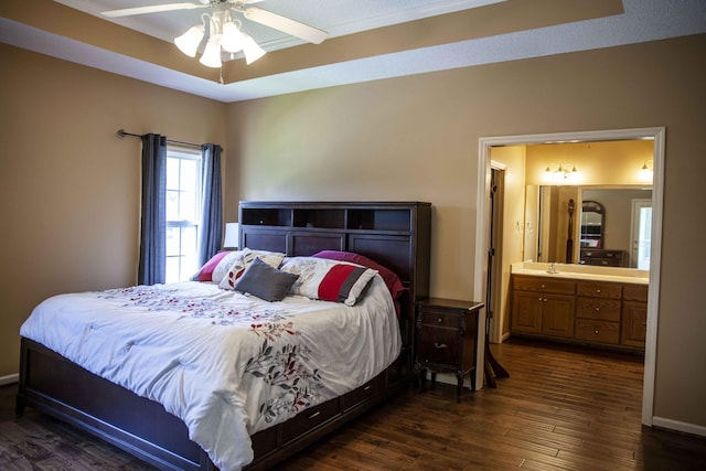 bedroom featuring dark hardwood / wood-style flooring, a tray ceiling, ensuite bath, and ceiling fan