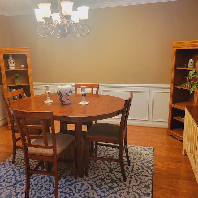 dining room featuring a chandelier, crown molding, light wood-type flooring, wainscoting, and a decorative wall