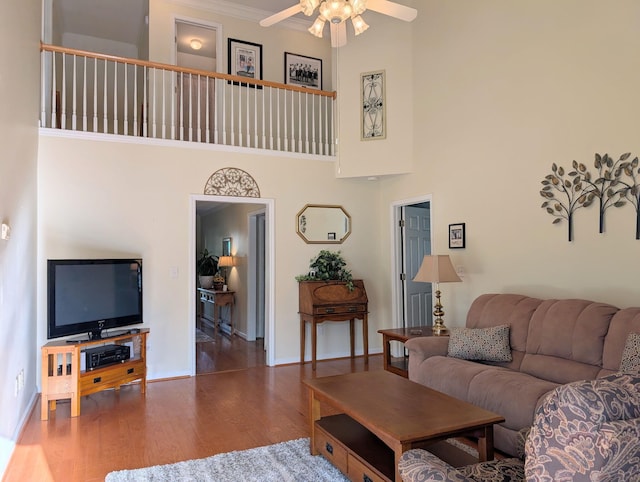 living area with a ceiling fan, wood finished floors, a towering ceiling, baseboards, and ornamental molding
