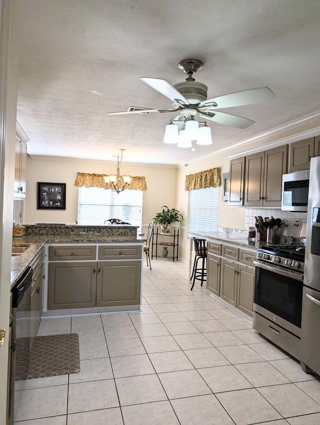 kitchen with stainless steel appliances, light tile patterned flooring, backsplash, a ceiling fan, and a chandelier