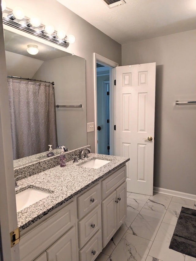 full bath with marble finish flooring, double vanity, and baseboards