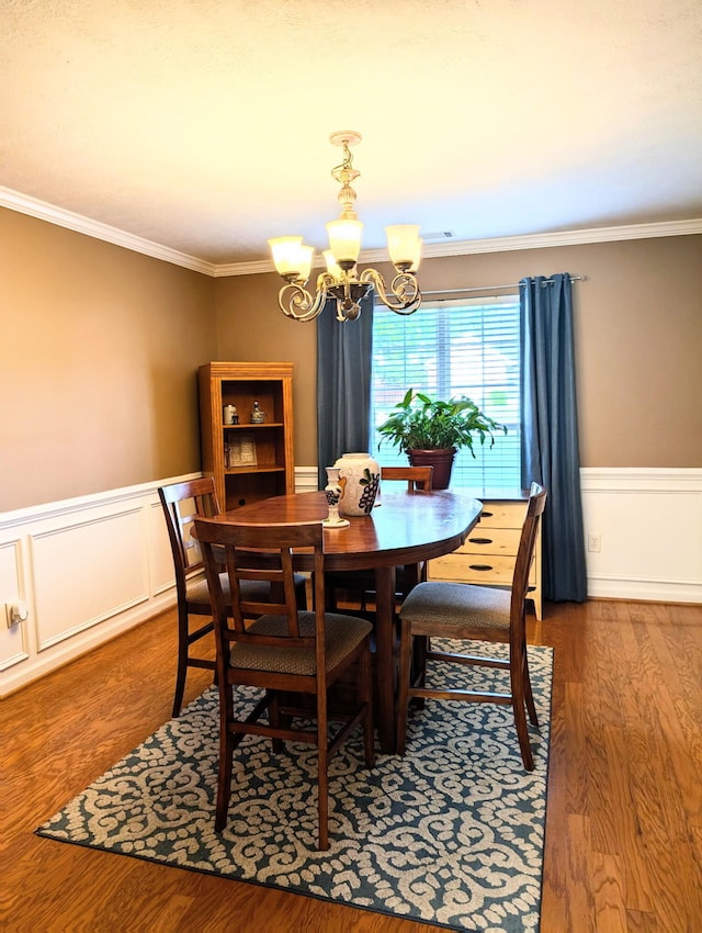 dining area featuring a chandelier, ornamental molding, wainscoting, and wood finished floors