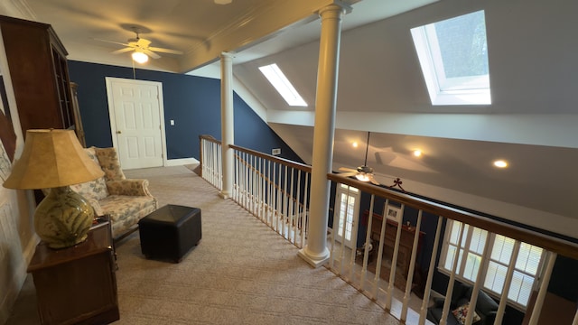 hallway with decorative columns, crown molding, vaulted ceiling with skylight, and light colored carpet