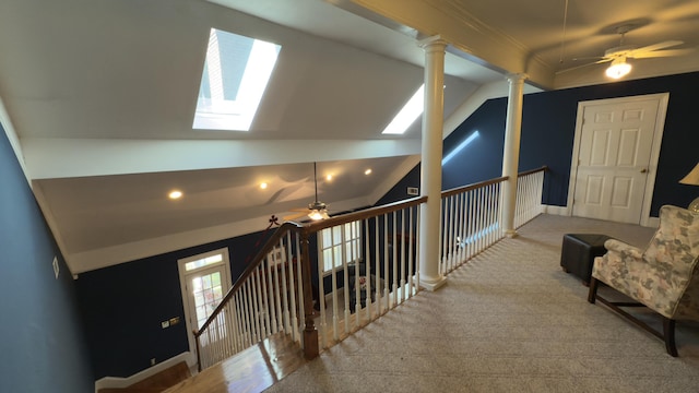 hall with ornate columns, vaulted ceiling with skylight, and light colored carpet