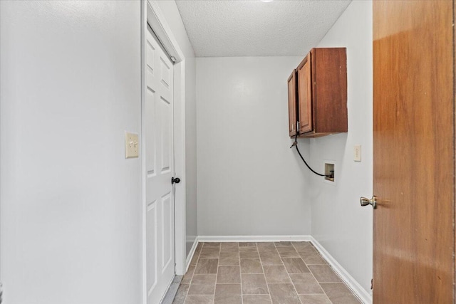 clothes washing area featuring hookup for a washing machine, a textured ceiling, cabinet space, and baseboards