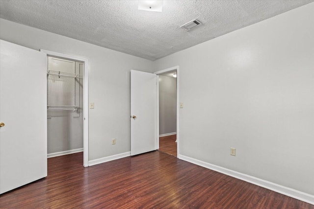 unfurnished bedroom with visible vents, a closet, baseboards, wood finished floors, and a walk in closet