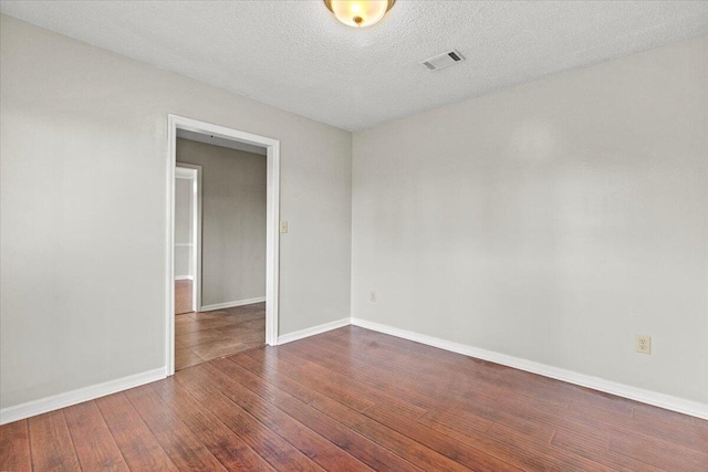 empty room with a textured ceiling, visible vents, hardwood / wood-style floors, and baseboards