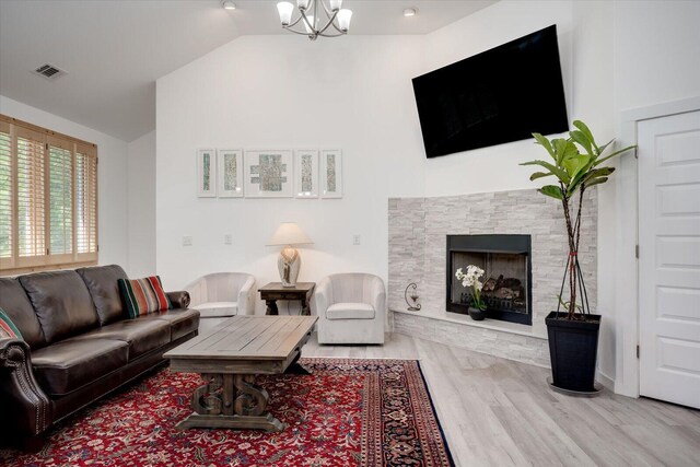 living room with a stone fireplace, light wood-type flooring, lofted ceiling, and an inviting chandelier