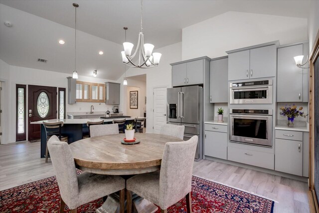 dining room with light wood-type flooring, high vaulted ceiling, a notable chandelier, and sink