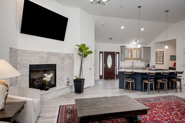 living room with a stone fireplace, sink, light hardwood / wood-style floors, and lofted ceiling