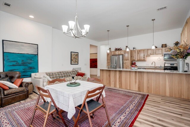 dining area featuring sink, a chandelier, and light wood-type flooring