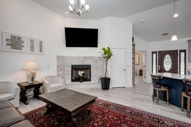 living room featuring a chandelier, light wood-type flooring, a stone fireplace, and lofted ceiling