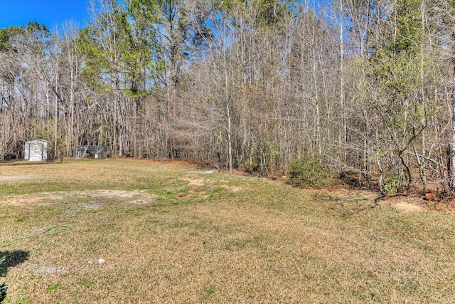 view of yard featuring an outdoor structure, a wooded view, and a shed