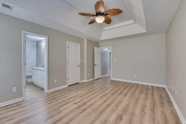 unfurnished bedroom with baseboards, visible vents, light wood-style flooring, ensuite bathroom, and a raised ceiling