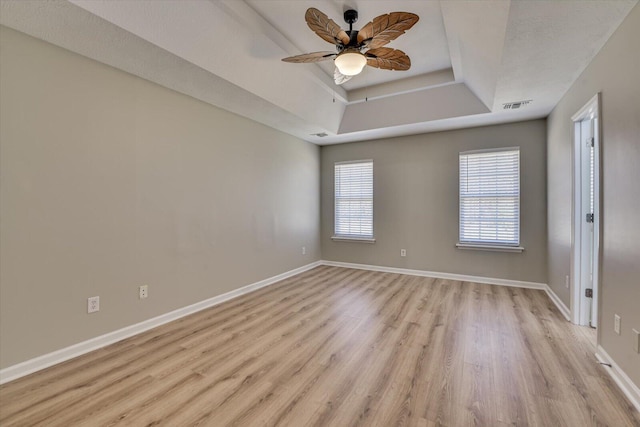 empty room featuring baseboards, visible vents, ceiling fan, a raised ceiling, and light wood-type flooring