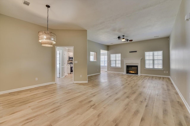 unfurnished living room featuring visible vents, baseboards, light wood-style floors, and ceiling fan with notable chandelier