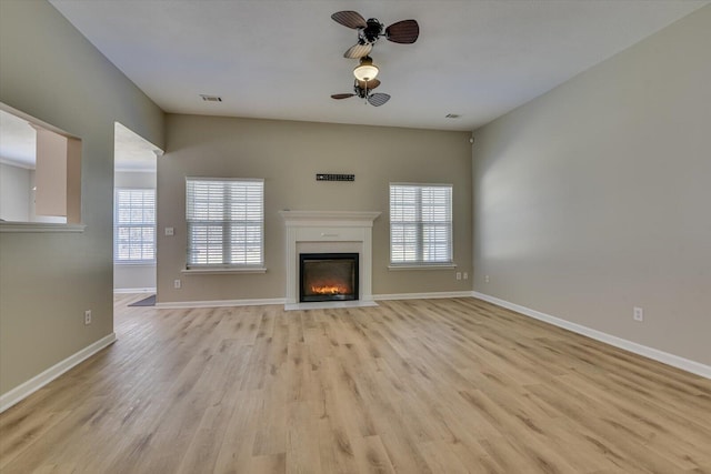 unfurnished living room with a glass covered fireplace, a ceiling fan, visible vents, and light wood finished floors