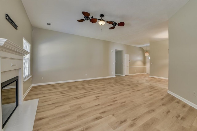 unfurnished living room with baseboards, light wood-style flooring, a tile fireplace, ceiling fan, and vaulted ceiling